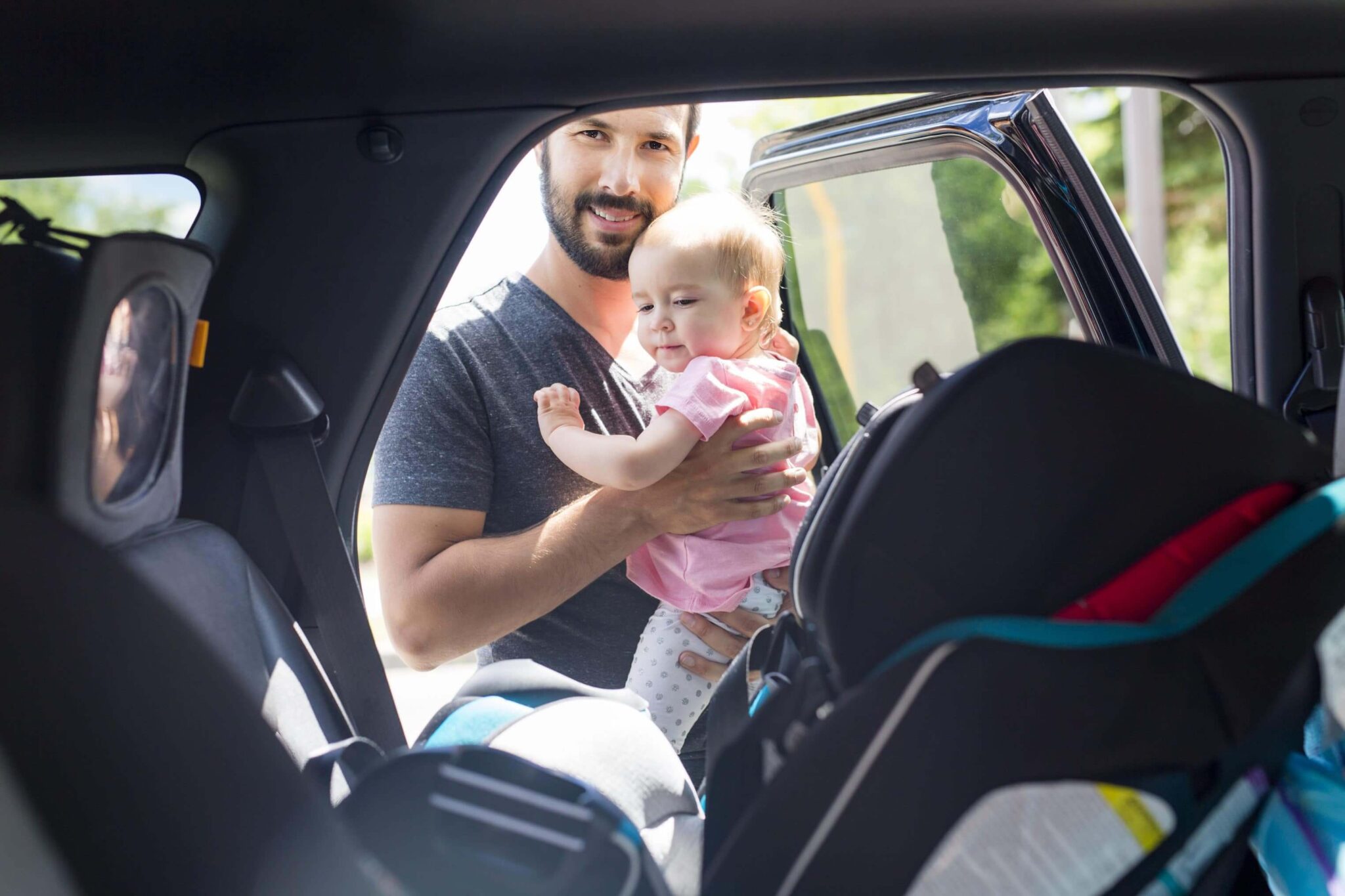 Happy man putting young child in a car seat