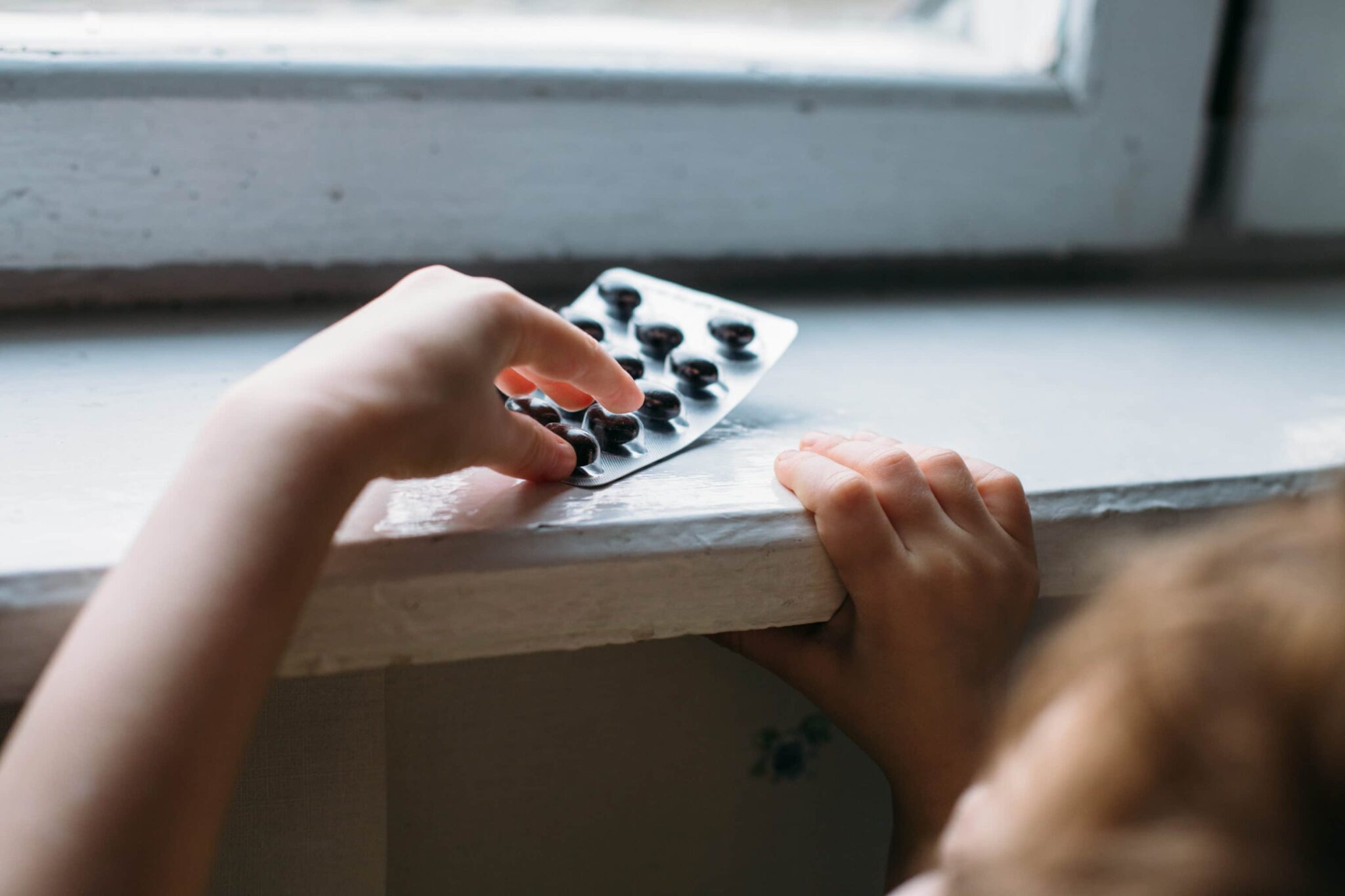 child's hands shown reaching up on a table for pills