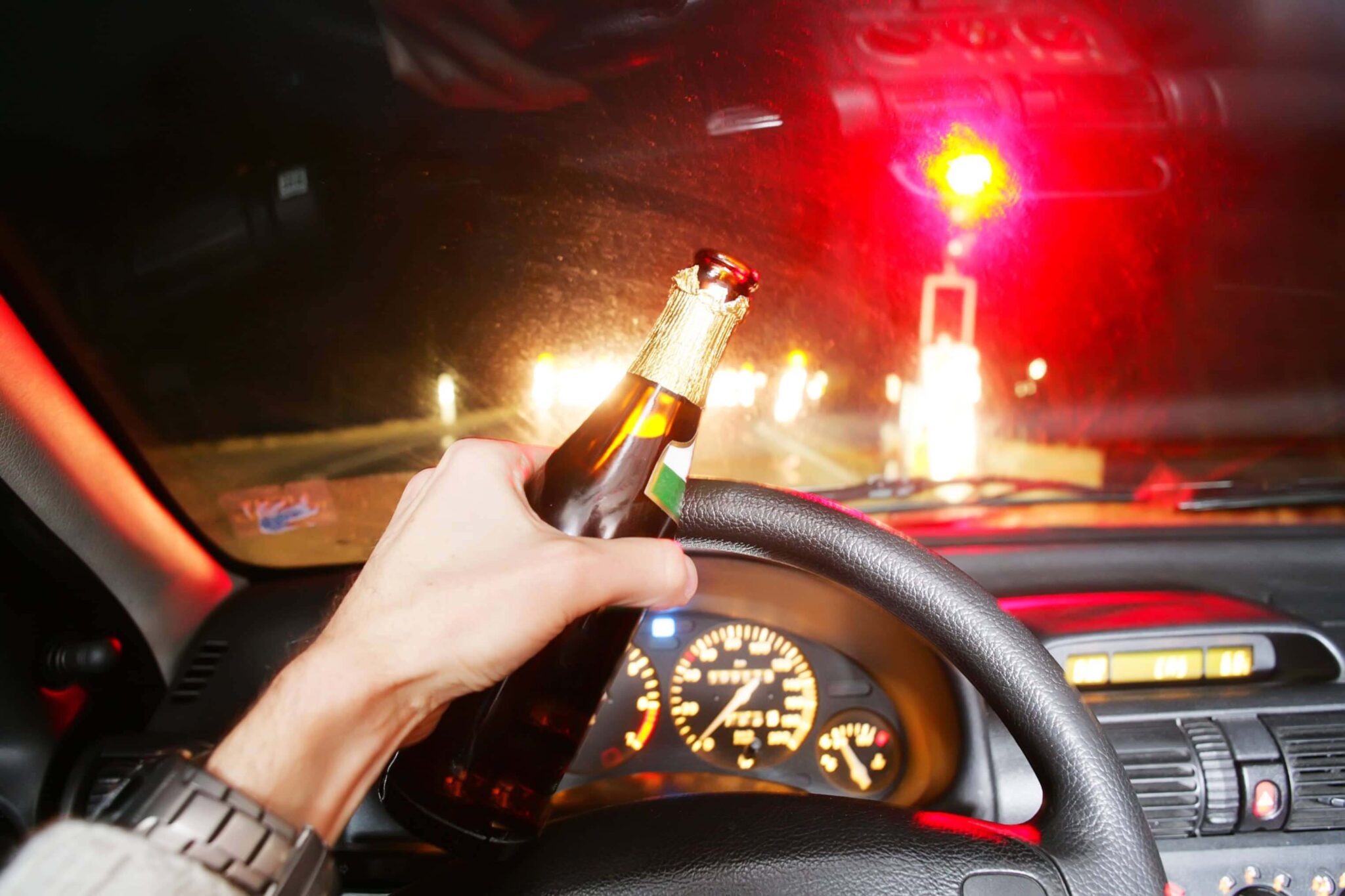 view of a steering wheel with driver's hand on it holding a beer