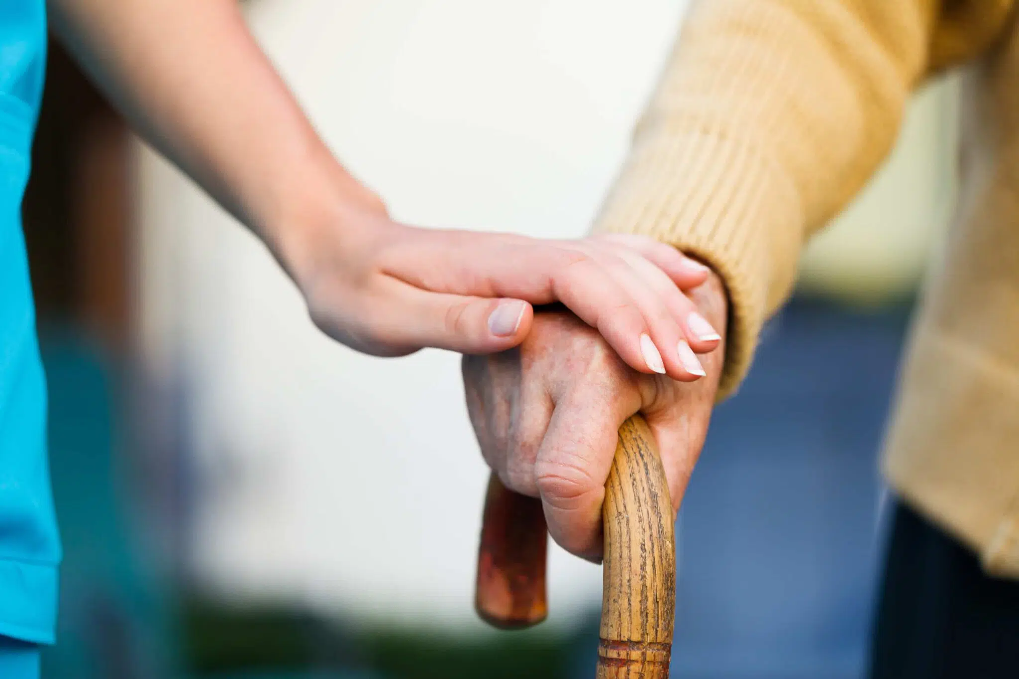 Young person's hand supporting the hand of an older person holding a cane