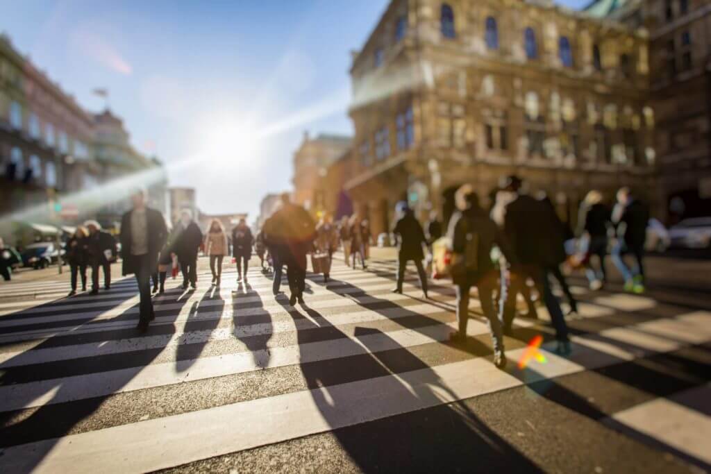 Blurred view of pedestrians crossing intersection with sun low in the sky in the background.