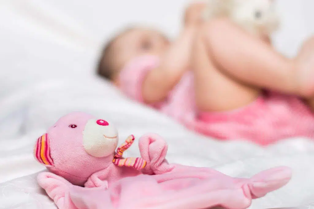 Pink stuffed animal in foreground with baby shown blurred in the background