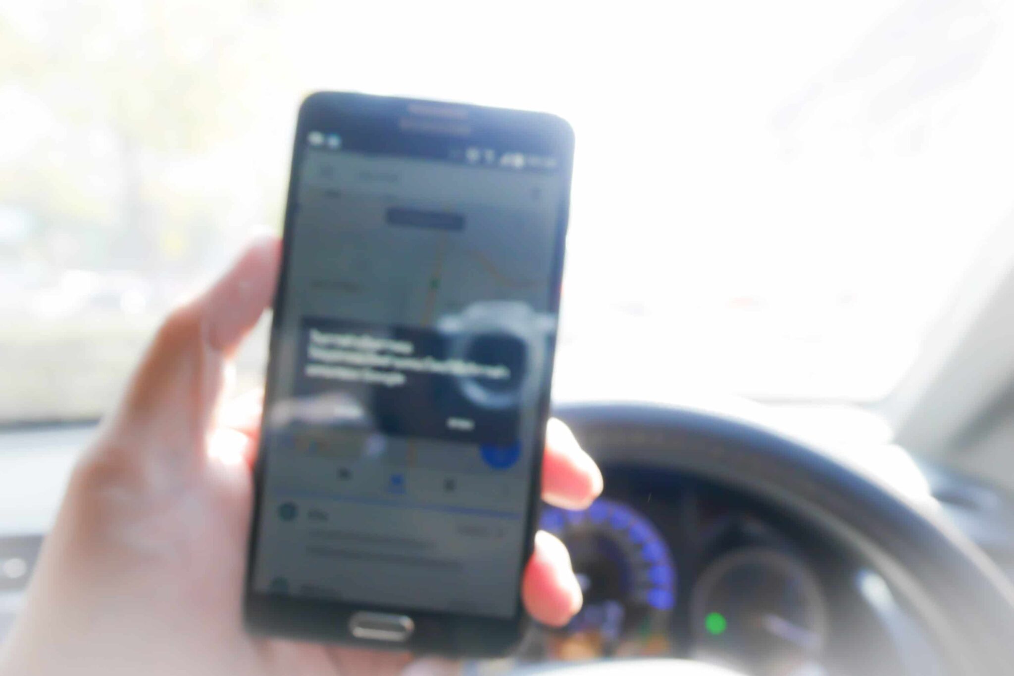 Driver's hand holding phone showing navigation software near the dashboard