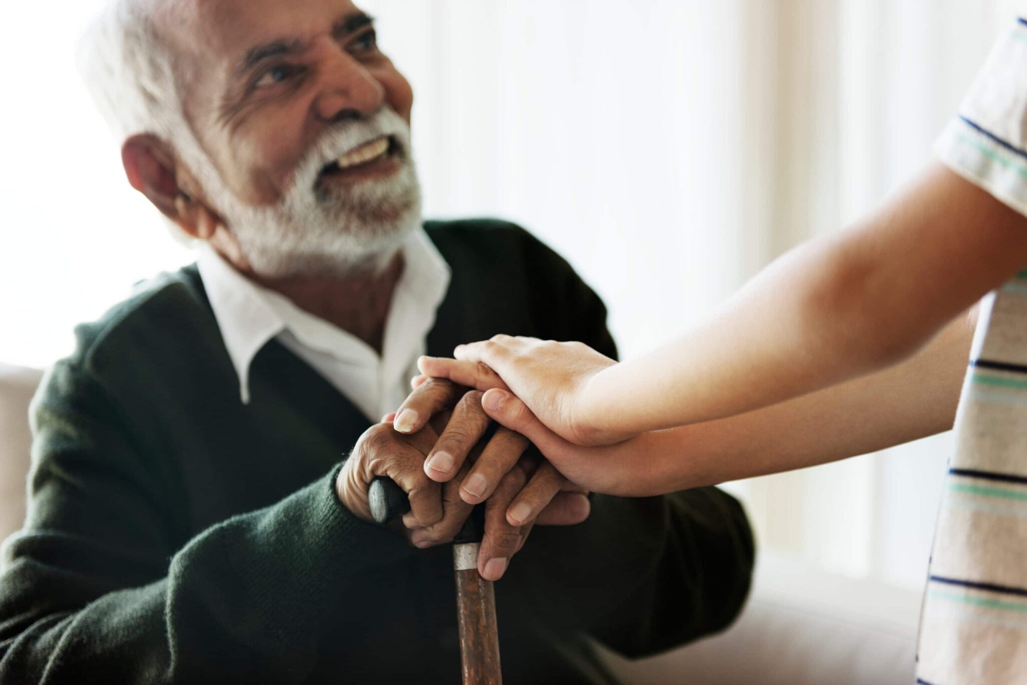 Child placing his hands over the hands of an older gentleman holding a cane