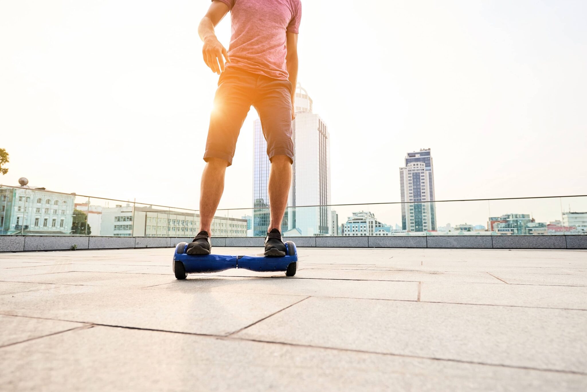 Young man riding on a hoverboard on the roof of a building with high-rise buildings shown in the background