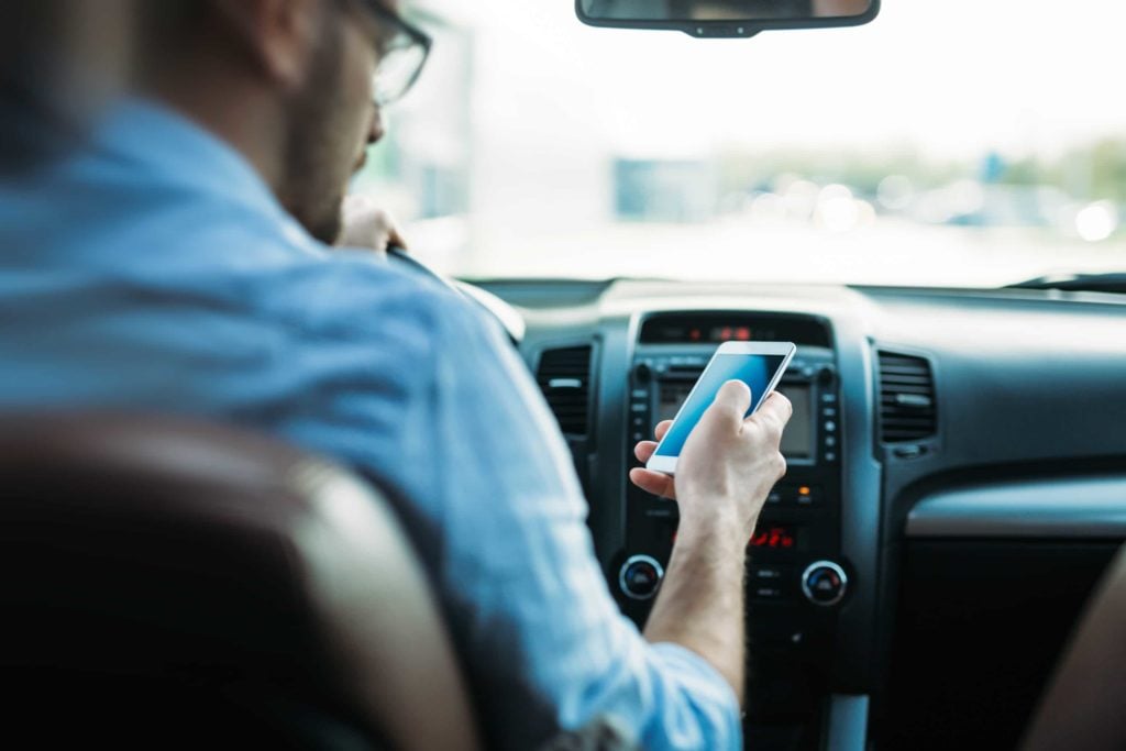 Man looking at smartphone while driving in a car