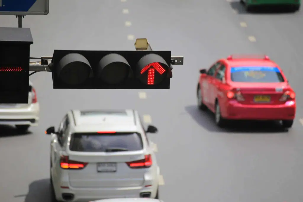 Red light arrow signal in foreground with cars driving below in the background