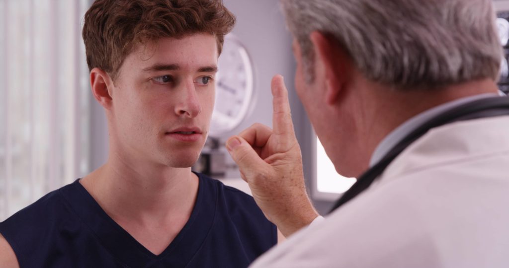 doctor holds up a finger in front of a young adult being tested for head injuries and a concussion
