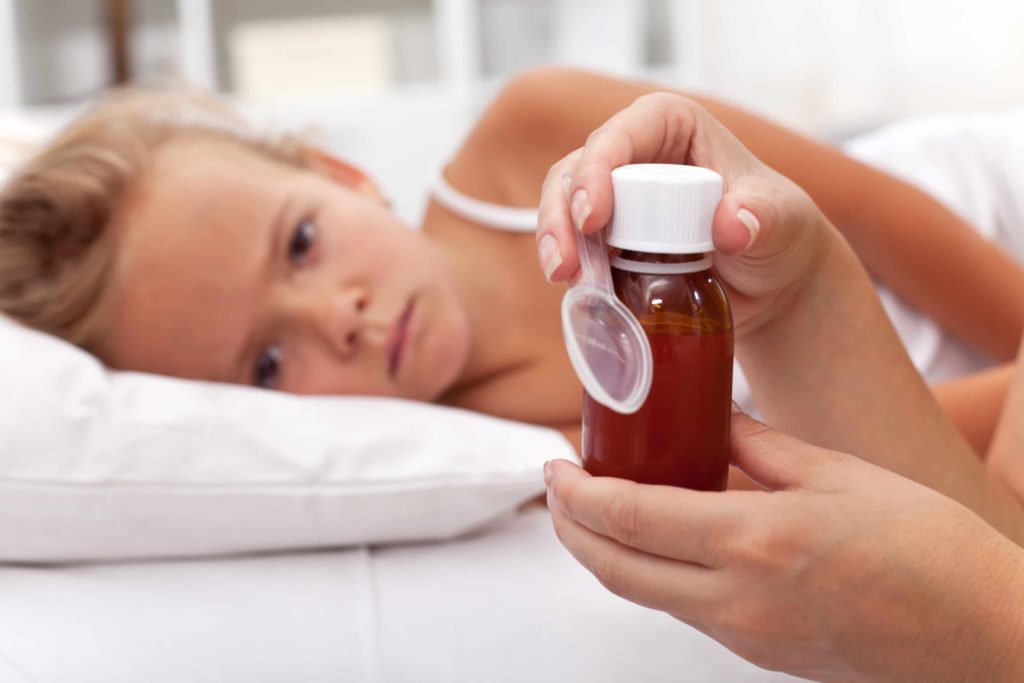 Sick daughter lies in bed while an adult gets ready to give her medication