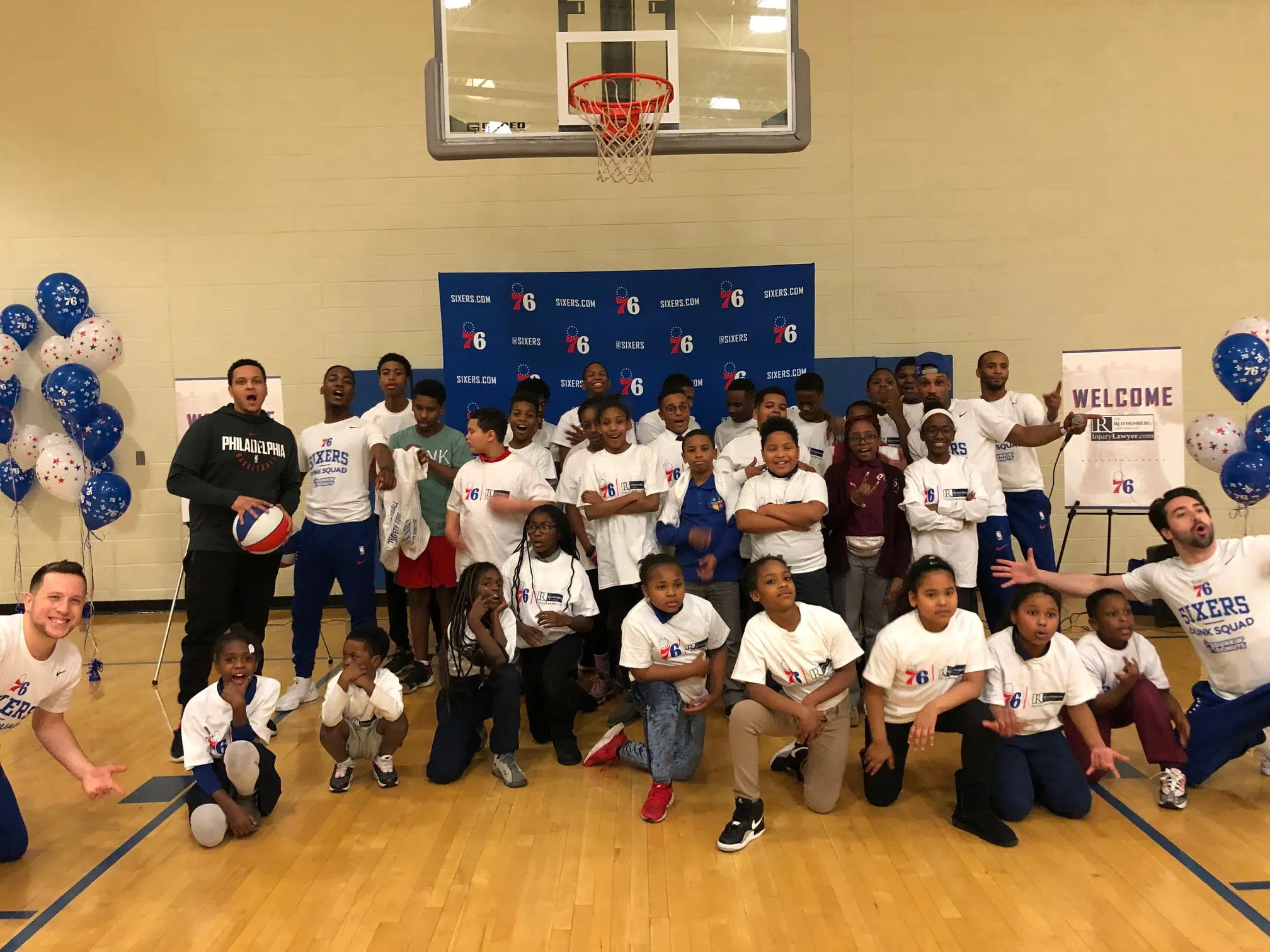 Children from the Chester, PA area pose for a picture under a basketball hoop with Philadelphia 76ers tee-shirts