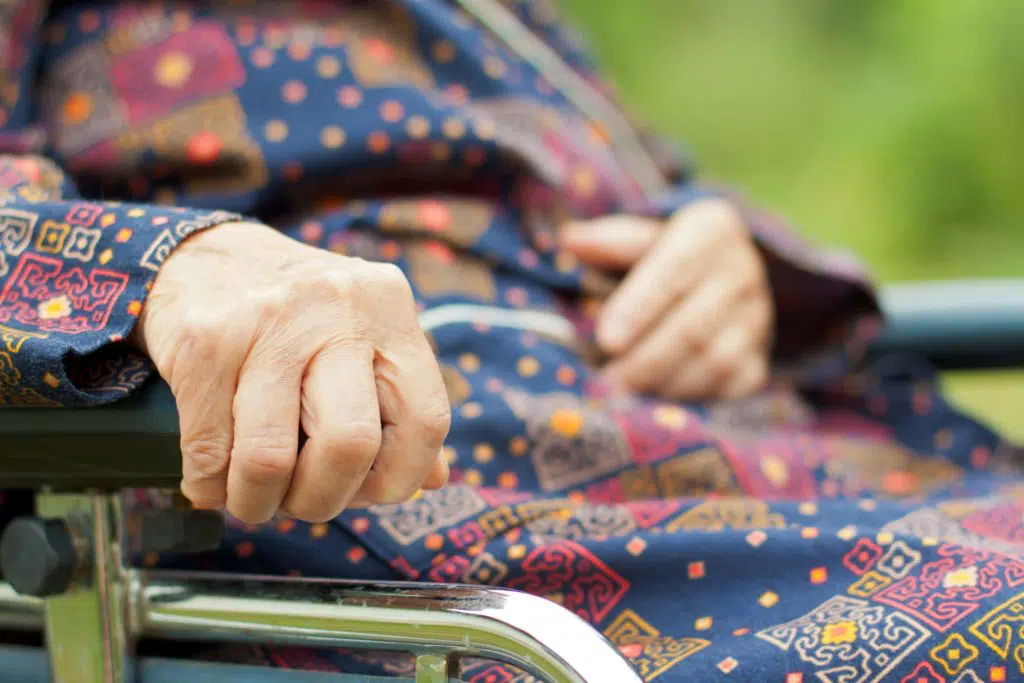 Hand of an older woman grips the arm rest of a wheelchair