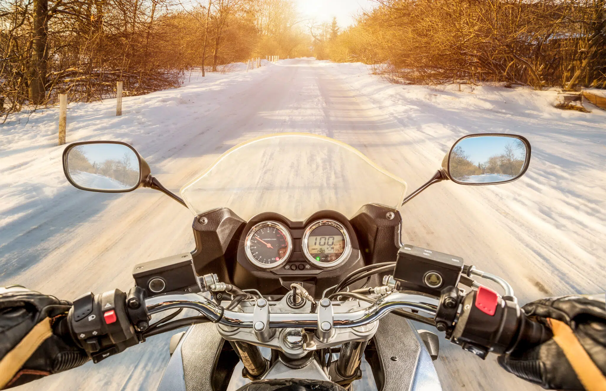 From the view of a motorcycle driver, a winter road covered in snow and the dashboard of a motorcycle.