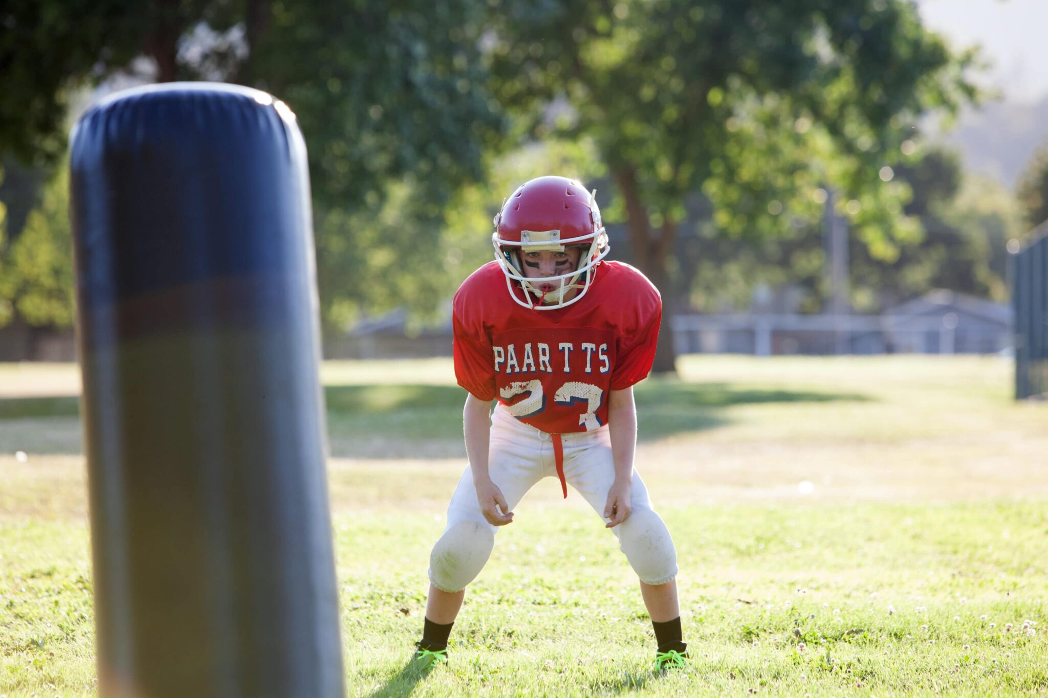 Pre-teen in lowered stance getting ready to tackle a dummy in football practice in a field.