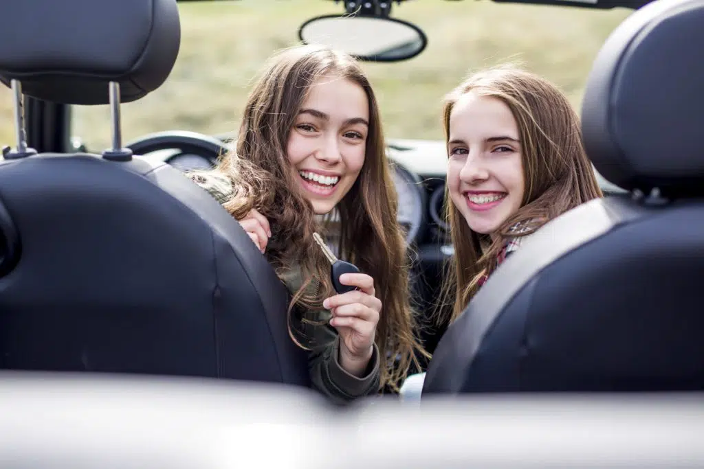 Two happy teenage girls in the driver and passenger seats showing off a set of keys
