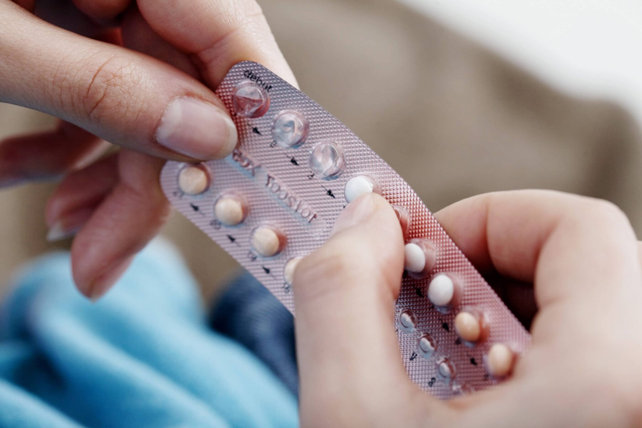 Hands hold a package of birth control pills, pressing their thumb into a blister on the first row of the package.