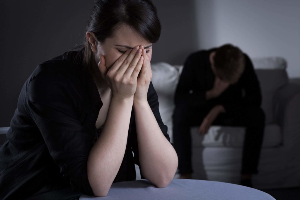 Woman and man mourning the death of a loved one in a dimly lit living room