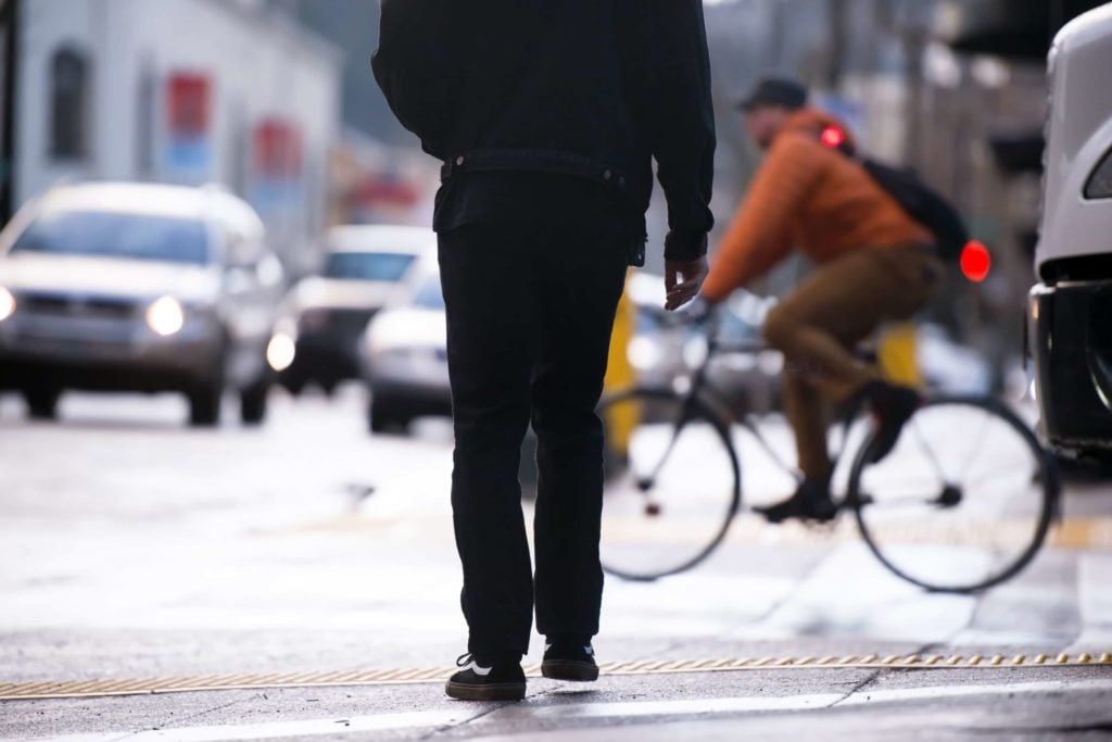 Pedestrian crossing the street with distracted cyclist riding in front of him.