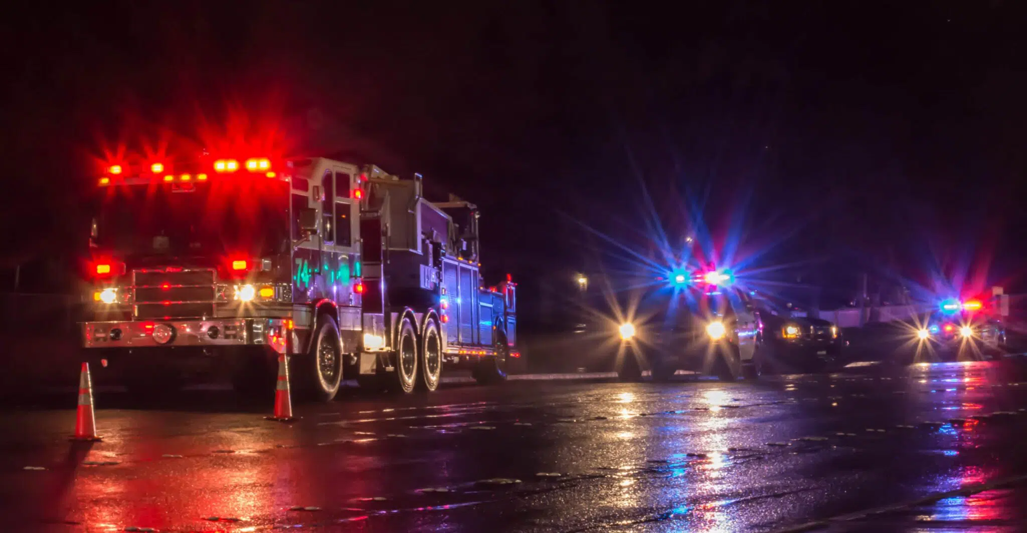 Fire trucks and emergency responder vehicles on a dar road on a rainy night.
