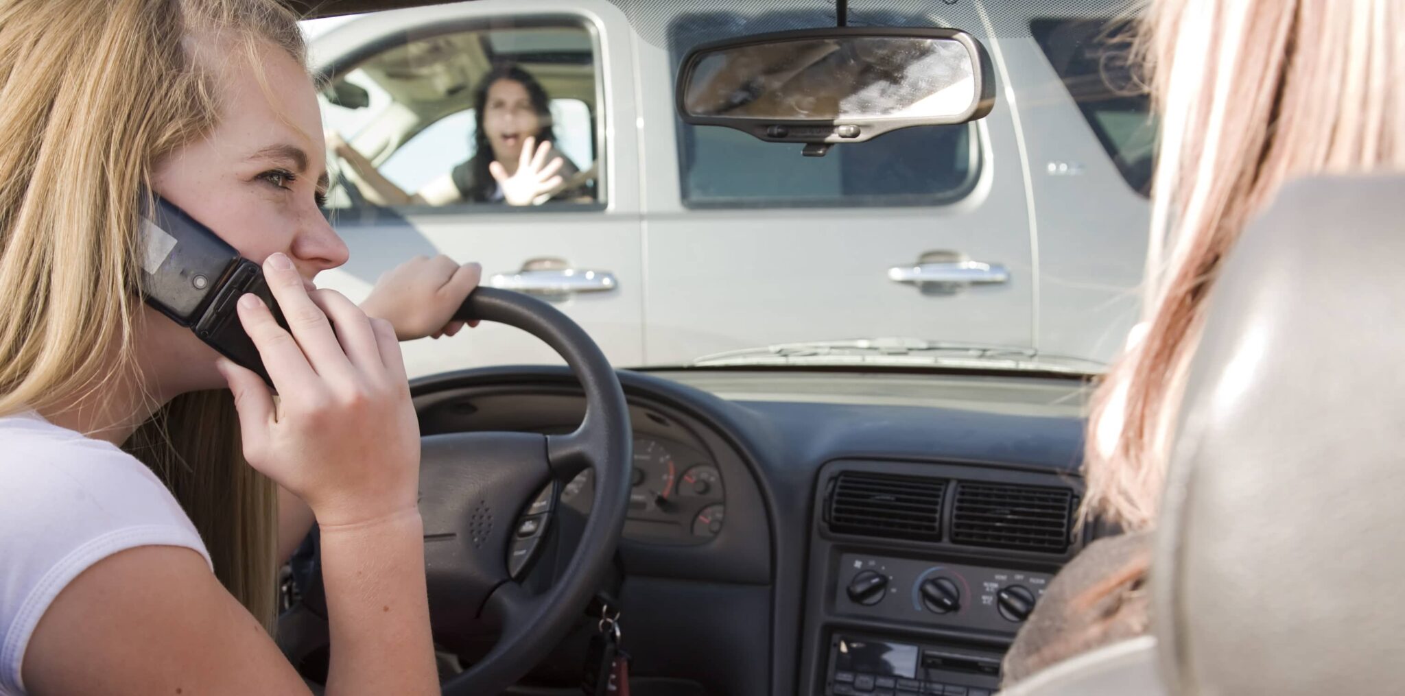 Girl talks on a phone and laughs with passenger as she dangerously approaches another driver who is in a vehicle waving her hand in front of her, fearing a collision