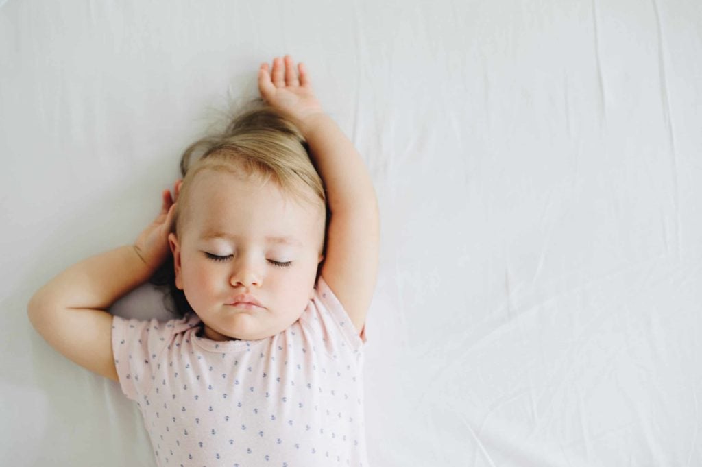 small child sleeping on a white sheet shown in aerial view