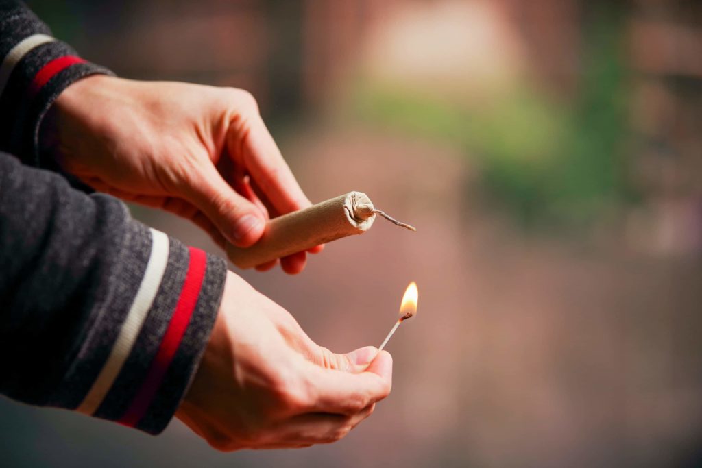 Man's hands shown lighting a small brown firewor