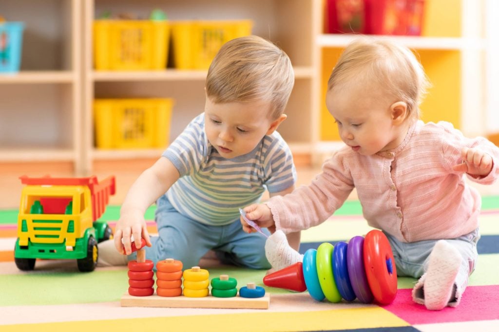 Happy babies playing with colorful toys on the floor of a daycare facility.