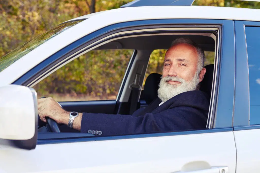 Older man with a gray beard behind the wheel in a vehicle.