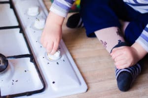 The hand of an unattended child is shown playing with the knobs of a stove.