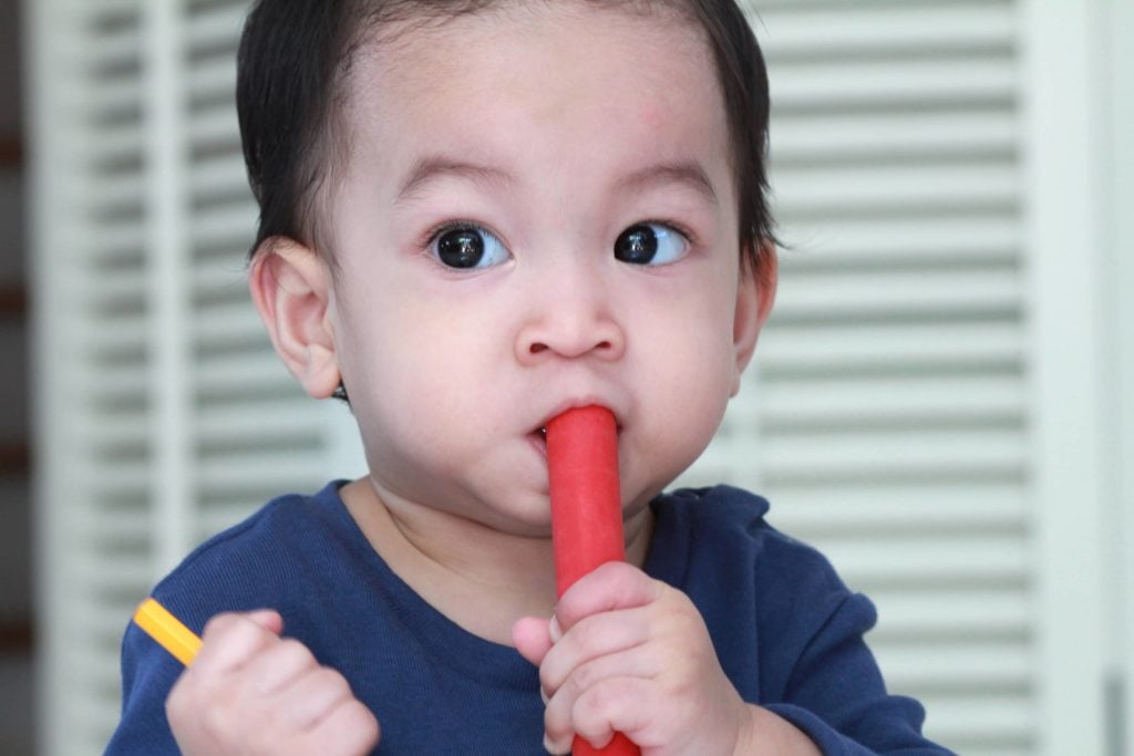 child with dark hair and eyes puts colored objects in his mouth