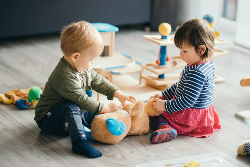 Two two-year-old children play on the floor at a daycare center