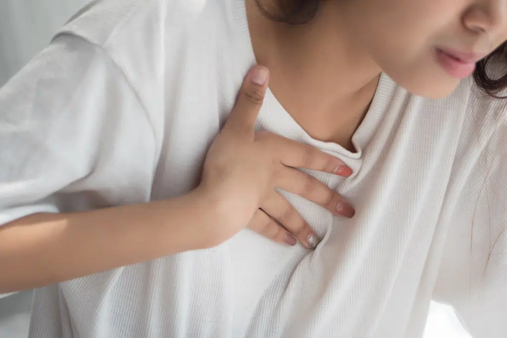 A young woman puts her hand on her upper chest with pain because she has heartburn