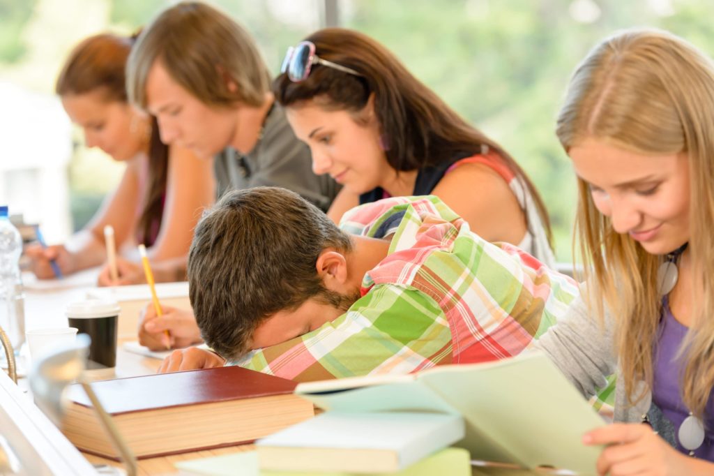 High school student puts his head down while other classmates happily do work around him