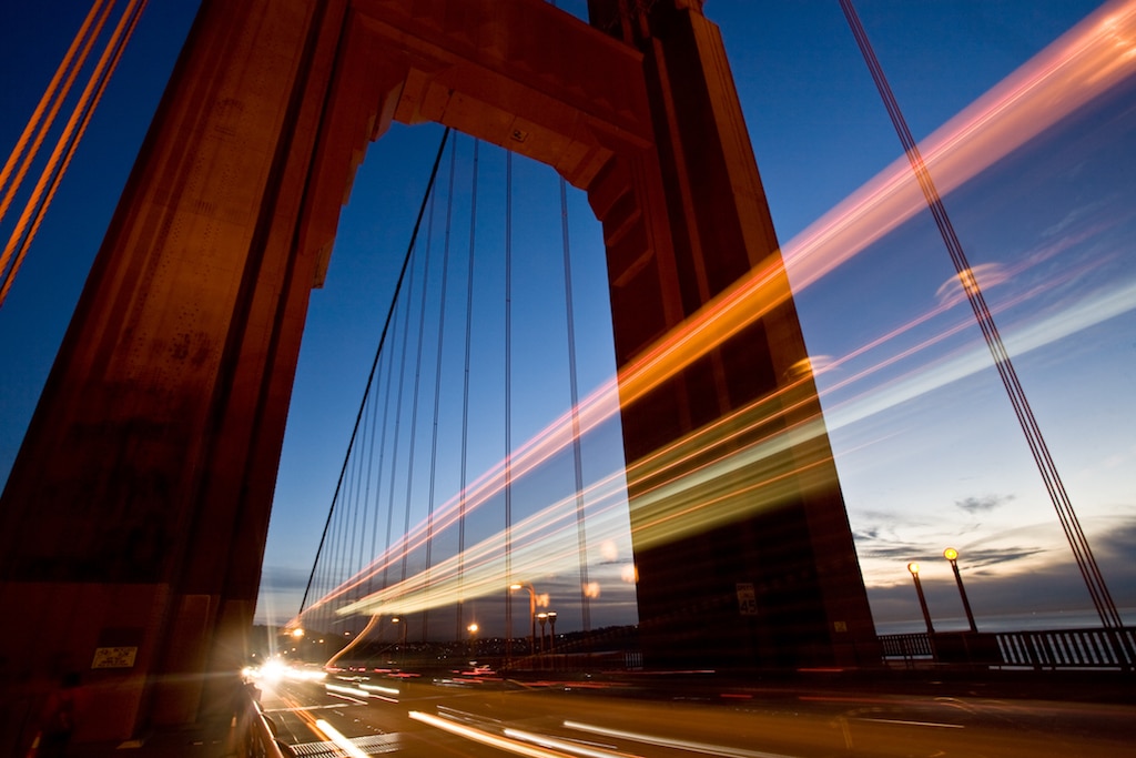 cars drive under a bridge at dusk