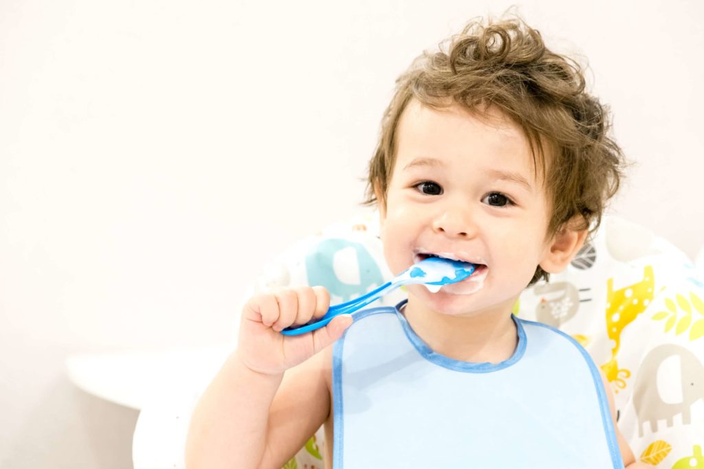 smiling child with a blue bib on puts a spoon in their mouth