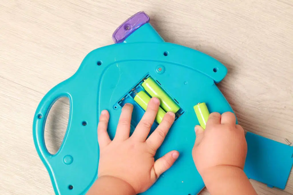 baby hands take batteries out of the back of a blue toy