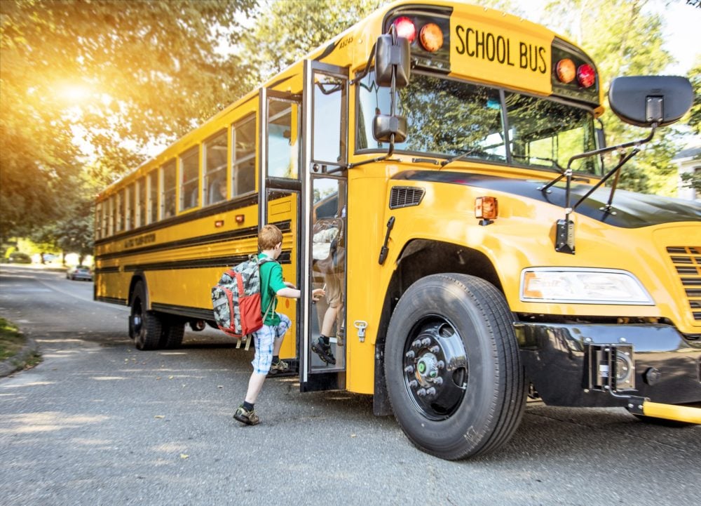 School-age child with colorful backpack boards yellow school bus