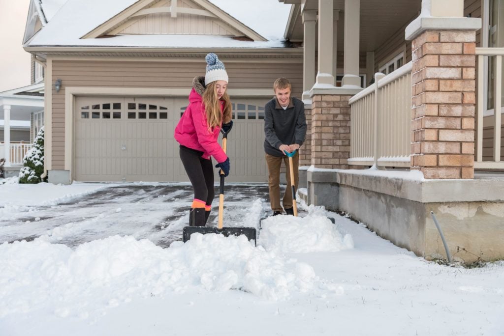 people shovel snow from a drive way next to a house