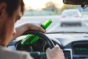 Drunk young man driving a car with a bottle of beer. Don't drink and drive concept. Driving under the influence. DUI, Driving while intoxicated. DWI