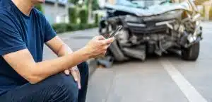Man calling with phone to his insurance agent after traffic accident with a background of the crashed car, Car insurance an non-life insurance concept.
