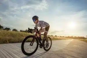 Cyclist riding bicycle on open road toward sunset.