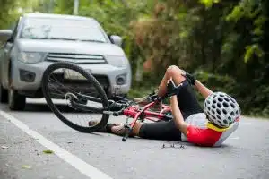 Mountain biker injured in collision with car on road. Concept emphasizes reducing car-related accidents. Selective focus.