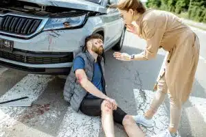 Concerned woman driver next to injured man at pedestrian crossing after road accident.