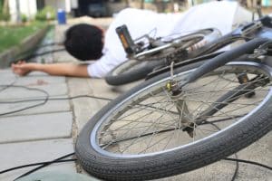 A man, shoes, and bicycle lying near a power pole after a crash across the road.