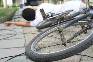 A man, shoes, and bicycle lying near a power pole after a crash across the road.