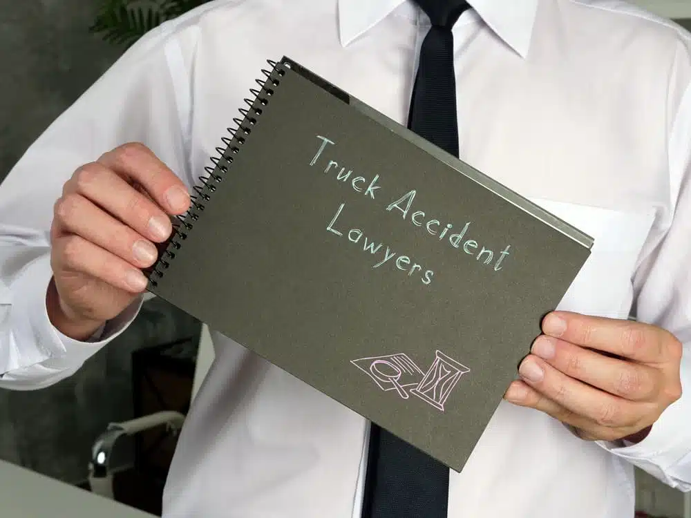 Man in business attire holding a notebook labeled "Truck Accident Lawyers".
