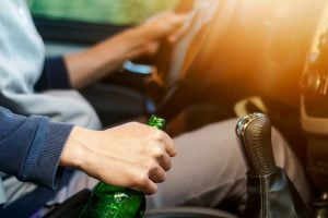 A man holding a alcohol bottle and drinking alcohol while driving a car.