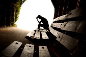 Silhouetted person sitting head in hands on park bench, conveying deep sadness.