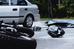 Crashed motorcycle and helmet on road with a car in the background.