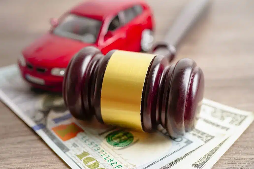 A gavel rests on money with a red toy car in the background, symbolizing legal settlements.