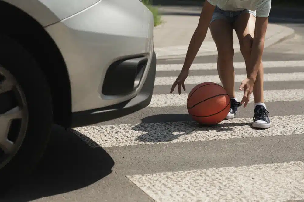 Close-up on kid with ball on pedestrian crossing next to car.